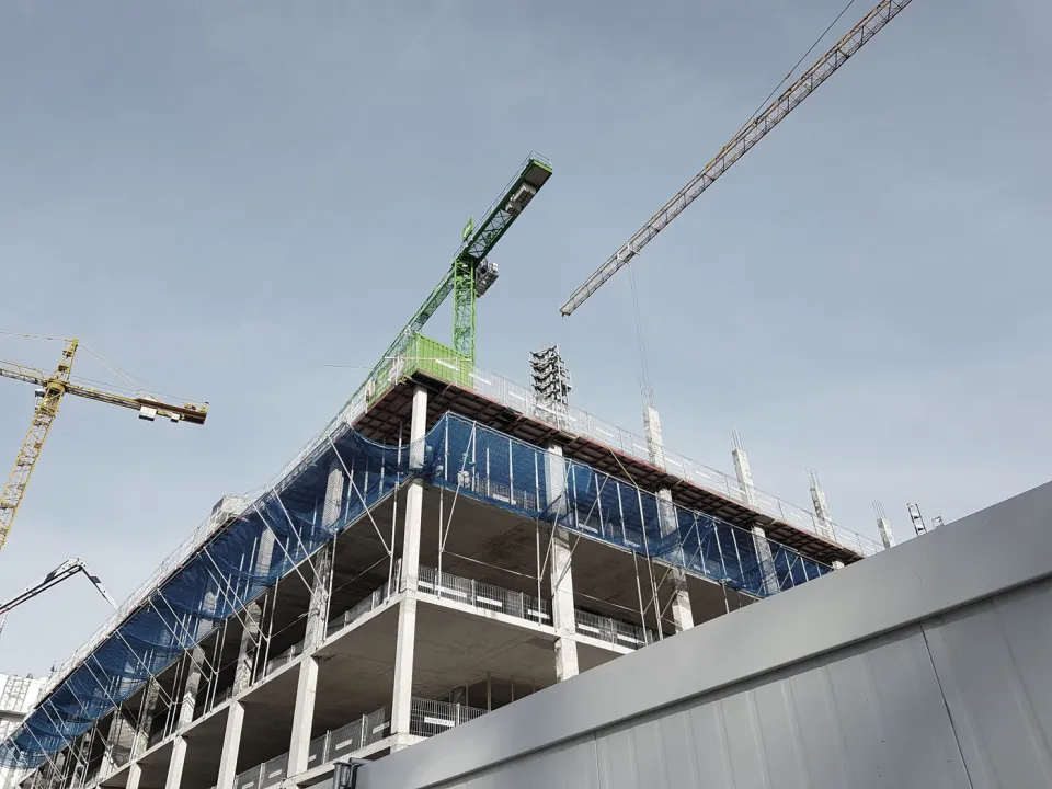 Mehrgeschossiger Rohbau mit blauem Gerüstnetz und Baukränen – Baustelle von MPG Marius Perseke Gerüstbau