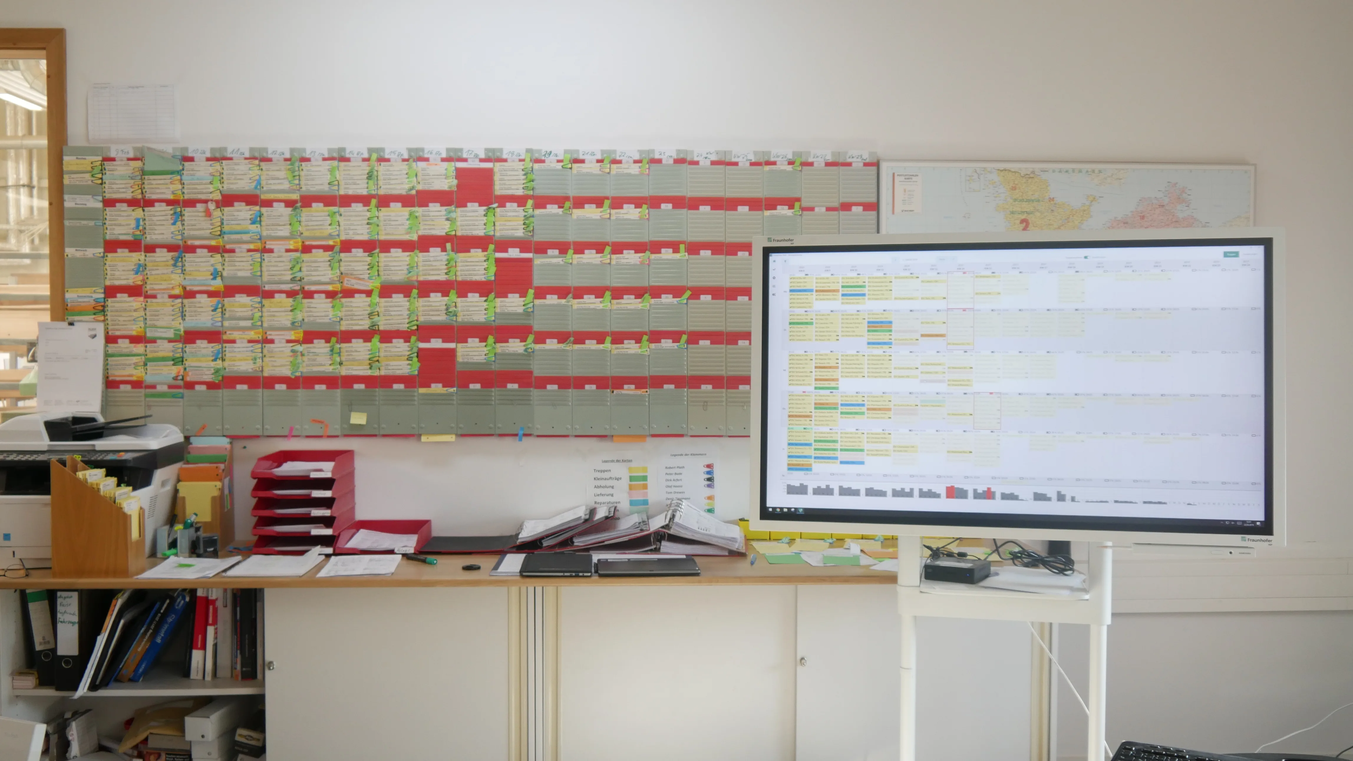 Analoge Steckkarten-Tafel neben dem Monitor mit der digitalen Plantafel im Büro bei Treppenbau Plath